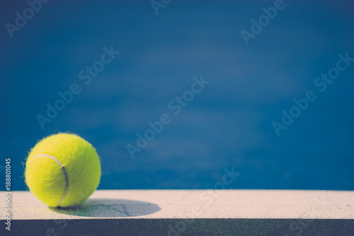 one new tennis ball on white line in blue hard court with light from left, shadow and copy space on right, vintage tone © angyim