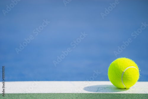 one new tennis ball on white line in blue and green hard court with light from right, shadow and copy space on left © angyim