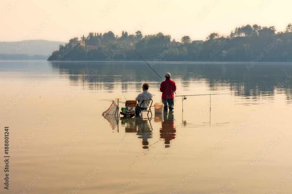 Two fishermen, immersed in the tranquil waters of a lake, are dedicated to sport fishing on a quiet summer afternoon Two fishermen, immersed in the tranquil waters of a lake, are dedicated to sport fishing on a quiet summer afternoon