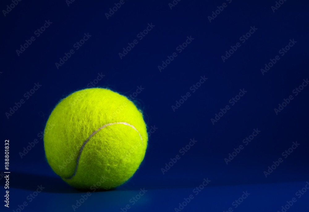 one new tennis balls on blue court with light from left, shadow and copy space on right, dark tone