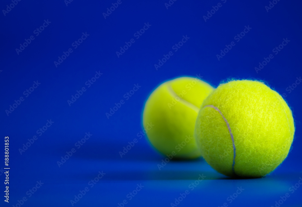 two new tennis balls on blue court with light from right, shadow and copy space on left