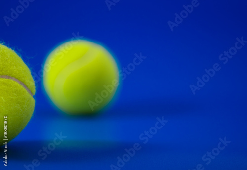 two new tennis balls on blue court with light from left, shadow and copy space on right © angyim