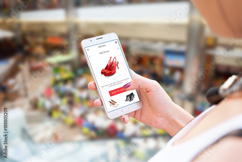 Shopping online with mobile phone. Woman holding smart phone. Shoes on app or web site. Shopping mall in background.