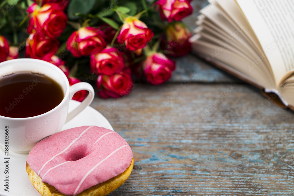 Cup of tea with donut, fresh roses and book  on a wooden background. Perfect image for mother's day