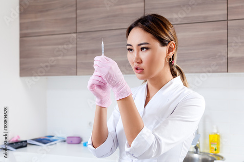 Close-up Young woman azite doctor beautician in white lab coat and sterile gloves prepares syringe for botox injection photo