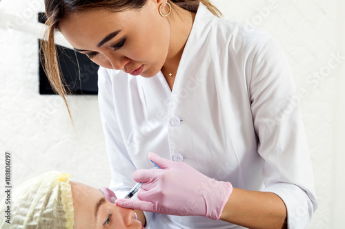 Close-up of a woman azian beautician in a medical dressing gown and sterile gloves makes a woman injecting Botox