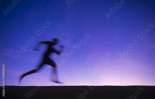 Silhouette blur of a runner passing across a purple twilight sunset sky background