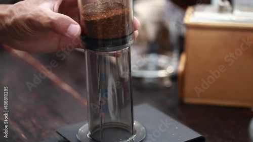 Barista make a cup of coffee, Aeropress model. Pouring hot water from teapot in aeropress pot with grounded coffee.