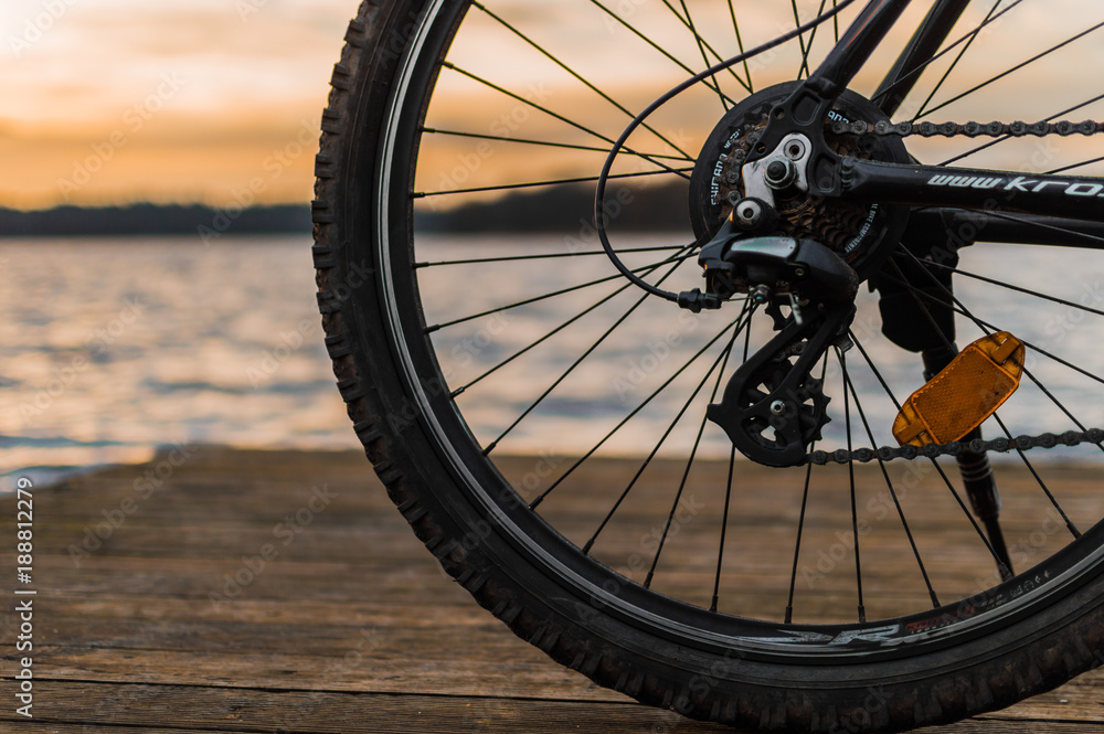 Mountain bike standing on a wooden bridge with lake and sunset in the background - selective focus