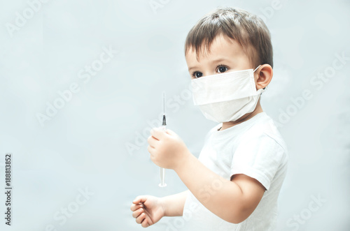 Child in a mask of the doctor with syringe in hands gray background photo