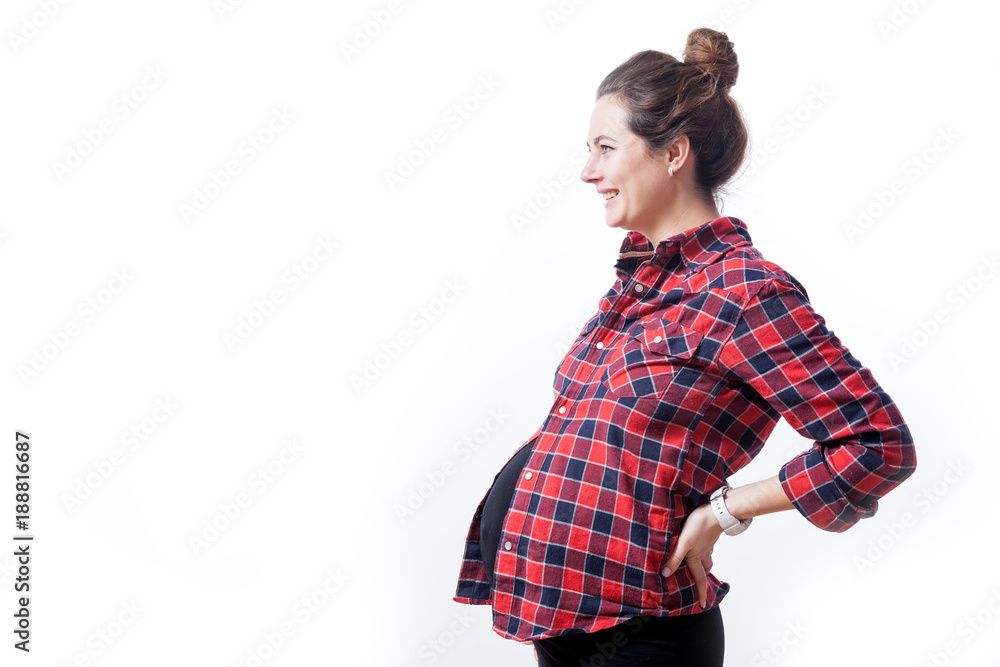 Young cheerful dark-haired woman in checkered shirt and black dress on late pregnancy smiles and supports herself behind her on a white isolated background Young cheerful dark-haired woman in checkered shirt and black dress on late pregnancy smiles and supports herself behind her on a white isolated background
