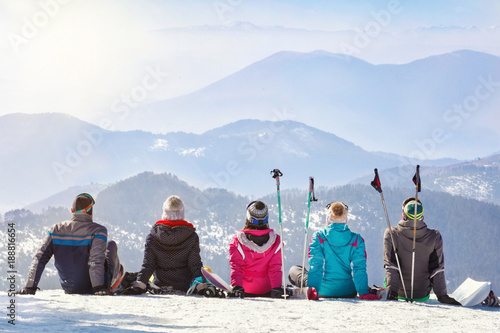 Skiers looking mountain hilles while sitting on snow, back view