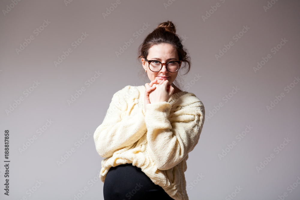 Portrait of a young dark-haired beautiful woman in her late pregnancy with glasses and a knitted milk-colored sweater on a white isolated background Portrait of a young dark-haired beautiful woman in her late pregnancy with glasses and a knitted milk-colored sweater on a white isolated background