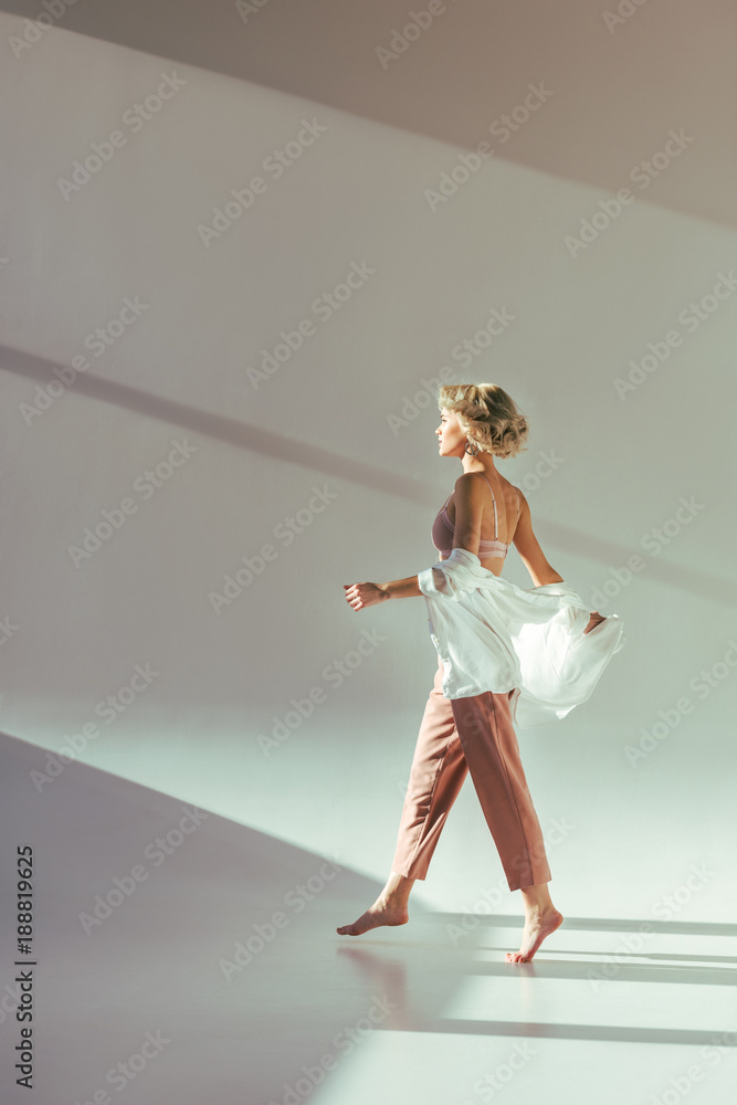 side view of barefoot blonde girl in pink bra, shirt and pants walking on grey
