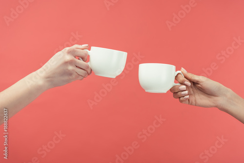 cropped view of women holding tea cups, isolated on red