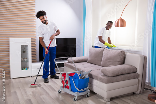 Smiling Two Young Male Janitor Cleaning The Living Room