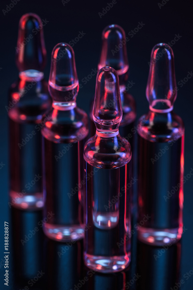 close up of five transparent glass ampoules with liquid on table on black close up of five transparent glass ampoules with liquid on table on black