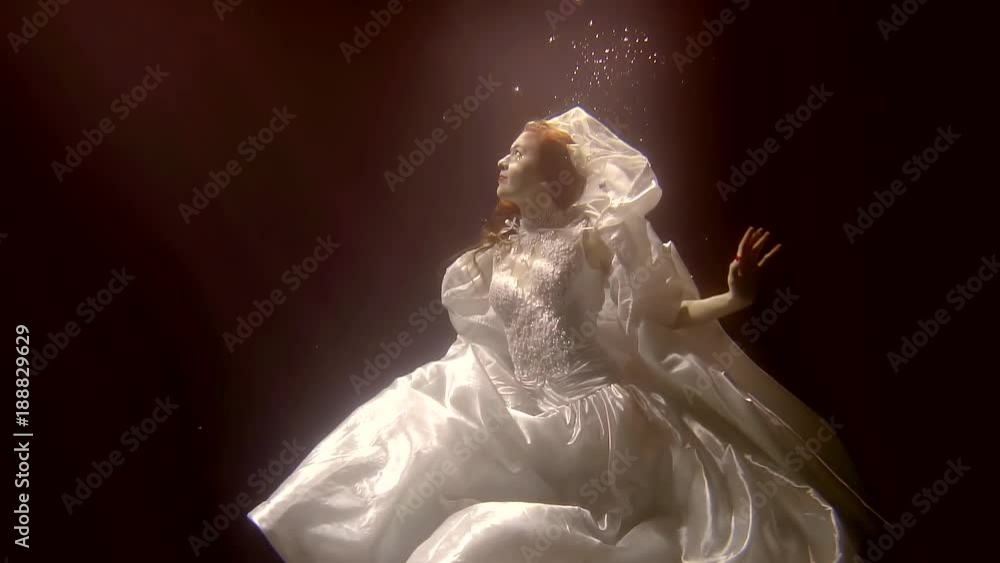 Wonderful woman is posing dressed in lovely wedding dress underwater