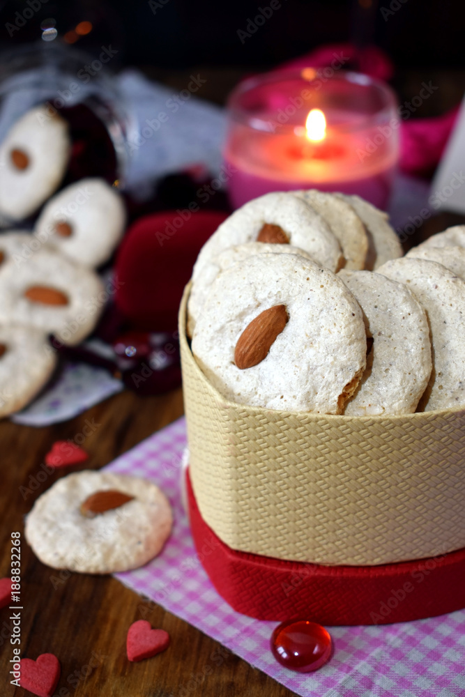 White cookies with almond in a heart-shaped box. Tiny hearts are scattered around. Treats for Valentine's Day White cookies with almond in a heart-shaped box. Tiny hearts are scattered around. Treats for Valentine's Day