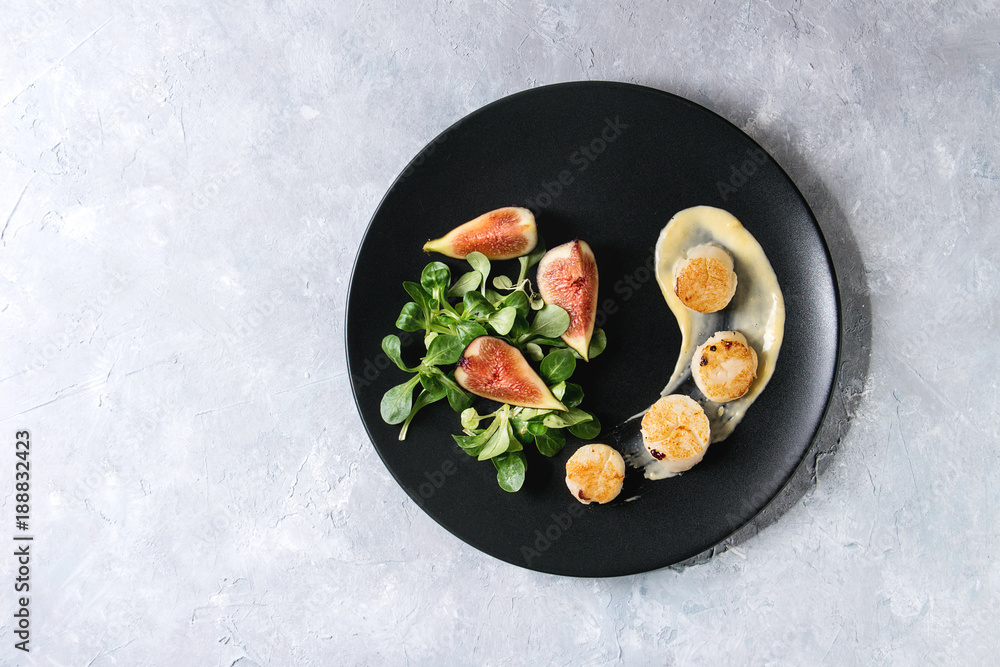 Fried scallops with lemon, figs, sauce and green salad served on black plate over gray texture background. Top view, copy space. Plating, fine dining - obrazy, fototapety, plakaty 