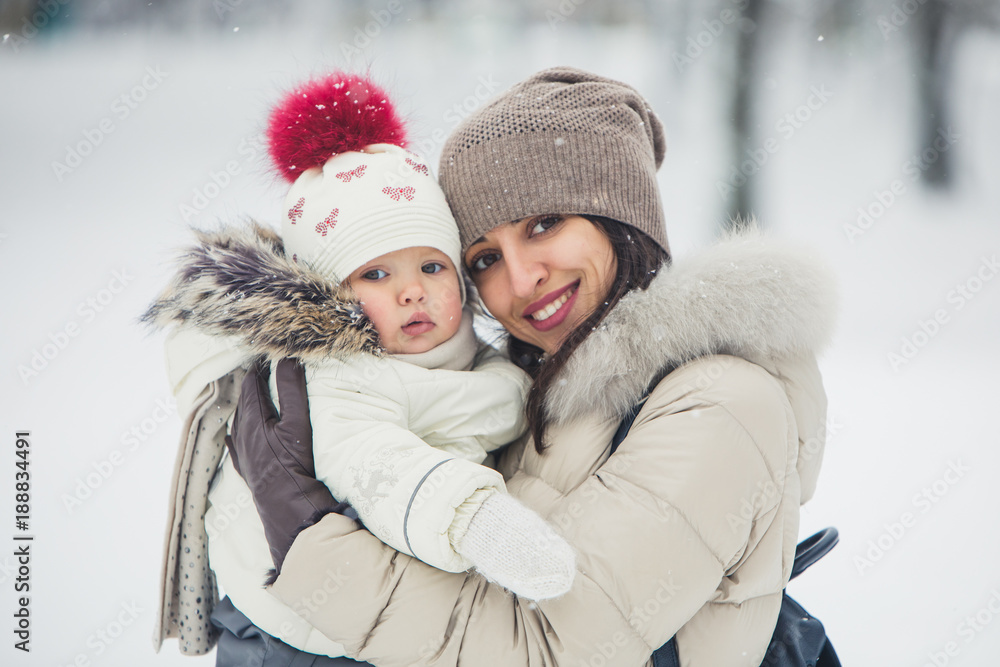 Close up brunette young women portrait with baby girl, daughter hugs and smiling in snowy park.