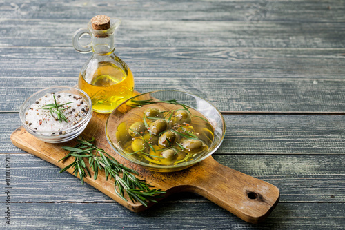 Olive oil in countess and olives with spices and fragrant herbs on a wooden background.