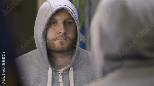 Drug paraphernalia to cover up drug use. Mirror reflected portrait of drug addicted man in hooded shirt using breathe spray near the mirror in bathroom. Drug abuse, addiction, social issues concept