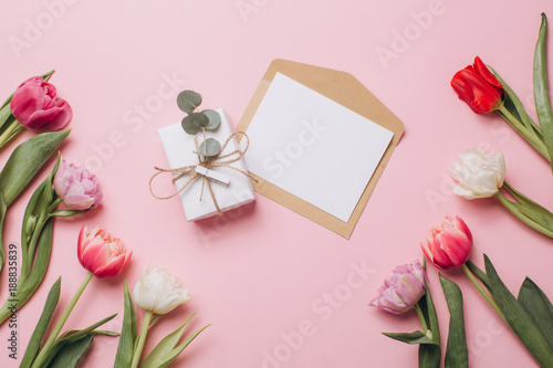 Gift and card on a pink background with tulips. Flat lay and top view.