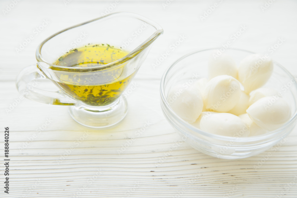 Preparing Food Concept with a jar of extra virgin olive oil and a bowl of mozarella cheese on a white wooden background, close up Preparing Food Concept with a jar of extra virgin olive oil and a bowl of mozarella cheese on a white wooden background, close up