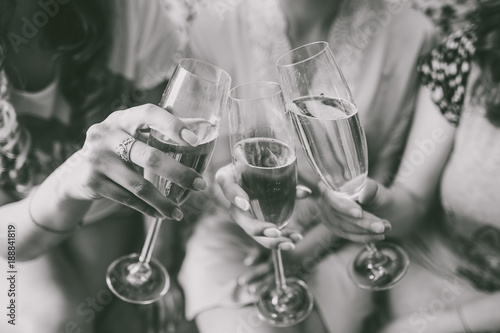 Closeup view of three female young hands holding wineglasses with champagne. Future bride with her girlfriends celebrating. Black and white photography.