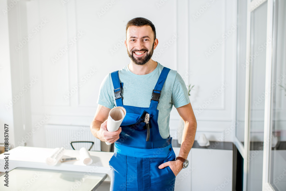 Portrait of a handsome repairman in the working uniform with paper drawings at the office Portrait of a handsome repairman in the working uniform with paper drawings at the office