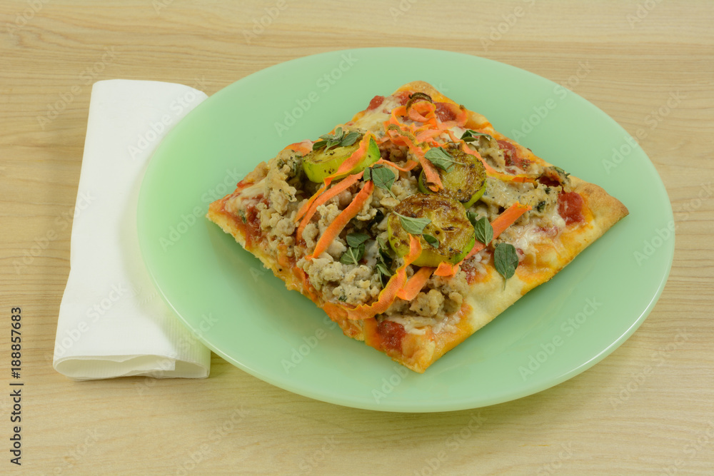 Homemade pizza with chicken sausage,zucchini and carrot toppings on green plate Homemade pizza with chicken sausage,zucchini and carrot toppings on green plate