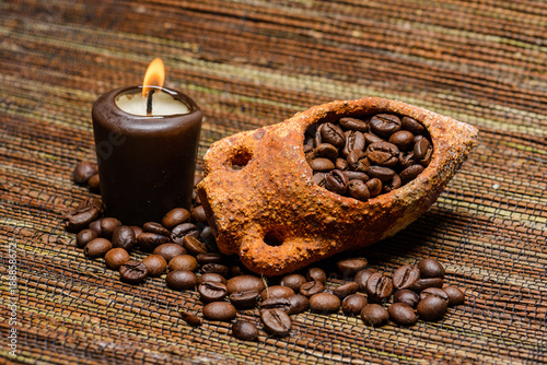 Pile of coffee beans in a smal amphora next to a burning canlde photo