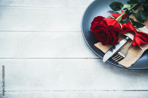 Fototapeta Naklejka Na Ścianę i Meble -  Festive table setting for Valentine's Day with fork, knife and rose on a white wooden table. Space for text. Top view.