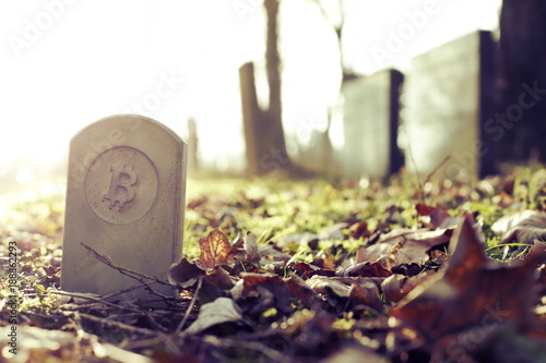 stone monument/tombstone with bitcoin symbol standing on cementery - vintage/chrome look - sunny blurred background - economic/financial concept