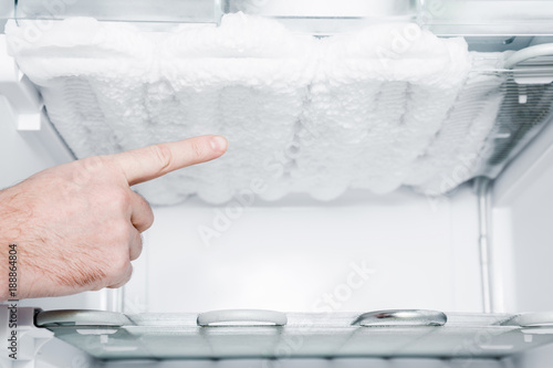 Man's hand pointing to the frozen ice in the empty freezer. Problem and solution concept.