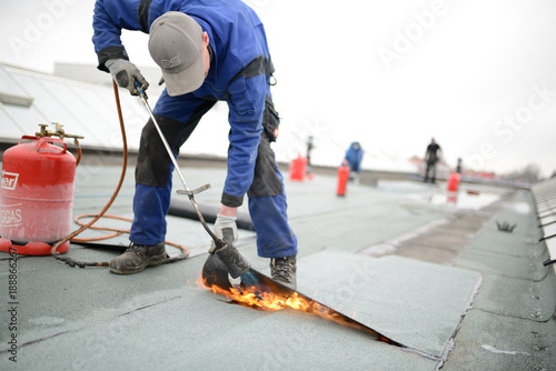 Flachdach Reparatur: Dachdecker verschweißt Dachabdichtung. Dachsanierung mit Gasbrenner. Immer Feuerlöscher vorhalten. photo