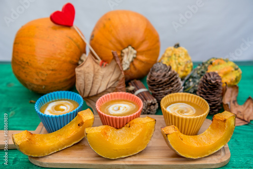 Pumpkin cream soup in colorful bowls with slices of roasted pumpkin and autumn/fall natural decorations, nature gifts