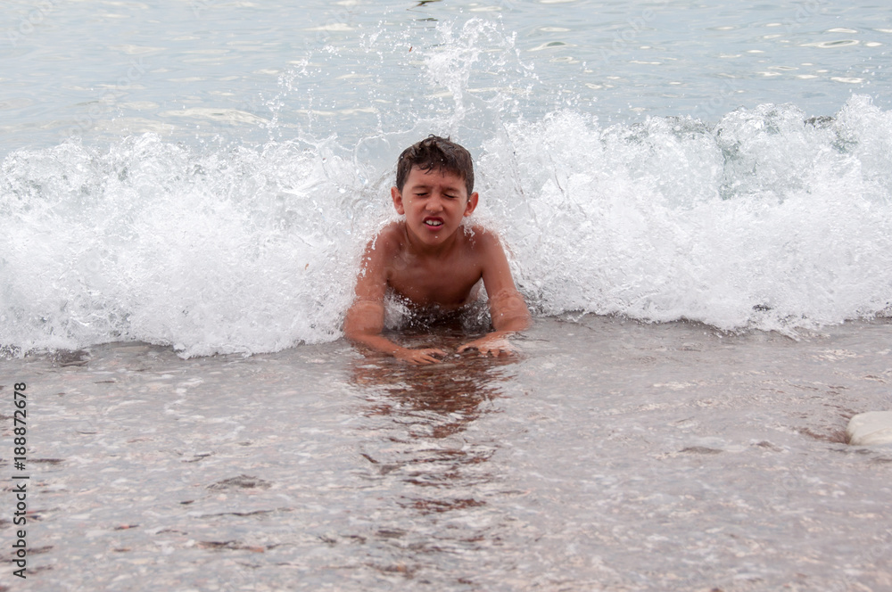 Young boy enjoying his summer vacation, swimming, and playing in the sea with waves splashing over him 