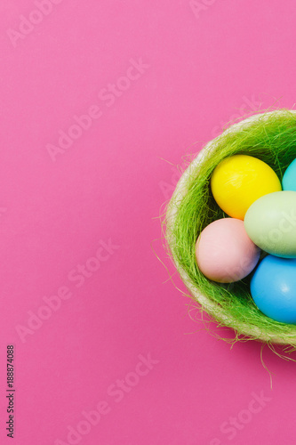 Vertical six colorful pastel painted Easter eggs in basket with green grass isolated on pink background. Happy Easter concept. Copy space for advertisement. With place for text. Top view on eggs.