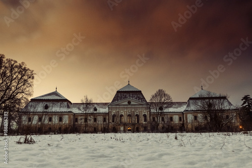 Medieval snowy castle in winter at night with beautiful orange - red sky. Creepy castle in Slovakia. European historic large castle in park.
