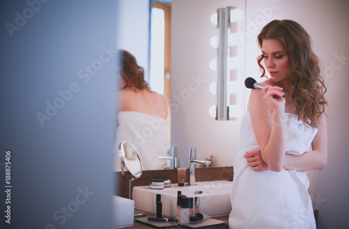 Young woman looking in the mirror and putting make-up on.
