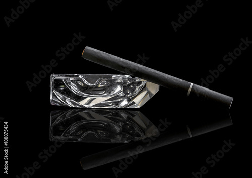 Single Kretek black clove cigarrete on a glass ashtray, black background and reflective surface. photo