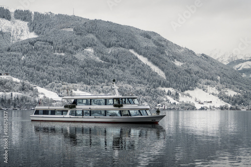 Tourist cruise in Austria (Zell am See) on frozen lake with snow and beautiful mountains on the background.  Tourist ship (boat) salling in winter time  and mirroring on the Zell am See lake