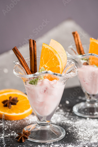 Vanilla Ice Cream With Fresh Mangoes on Black plate. Ice cream dessert, yogurt with orange slices, green mint leaves, cinnamon sticks on a dark stone tray and gray concrete background. photo