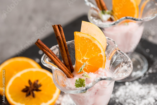 Vanilla Ice Cream With Fresh Mangoes on Black plate. Ice cream dessert, yogurt with orange slices, green mint leaves, cinnamon sticks on a dark stone tray and gray concrete background. photo