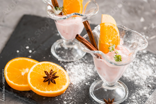 Vanilla Ice Cream With Fresh Mangoes on Black plate. Ice cream dessert, yogurt with orange slices, green mint leaves, cinnamon sticks on a dark stone tray and gray concrete background. photo