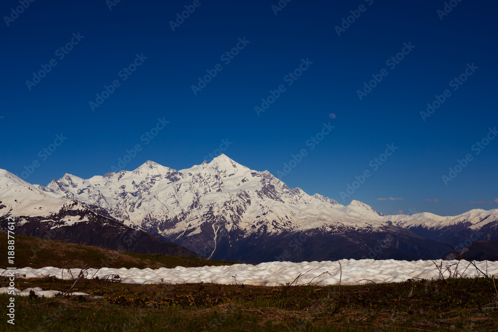 Fototapeta premium Pale moon rises over the snow-covered mountain ridge