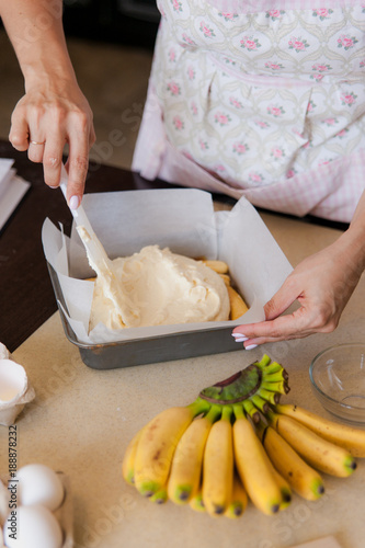 Female hands spreads dough in a baking dish. Cooking process on kitchen. Ingredients for sweet fruit dessert on table.