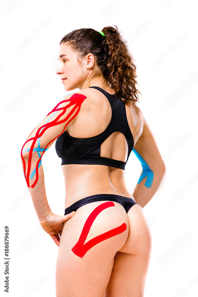sexy female athlete with beautiful booty stands half sideways on white  background in black top and bikini.On body is pasted kinesiology tape.Colored  tapes for treatment of muscles,tendons in athletes Stock Photo